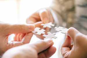 Four hands each holding a jigsaw piece coming together | NICRC